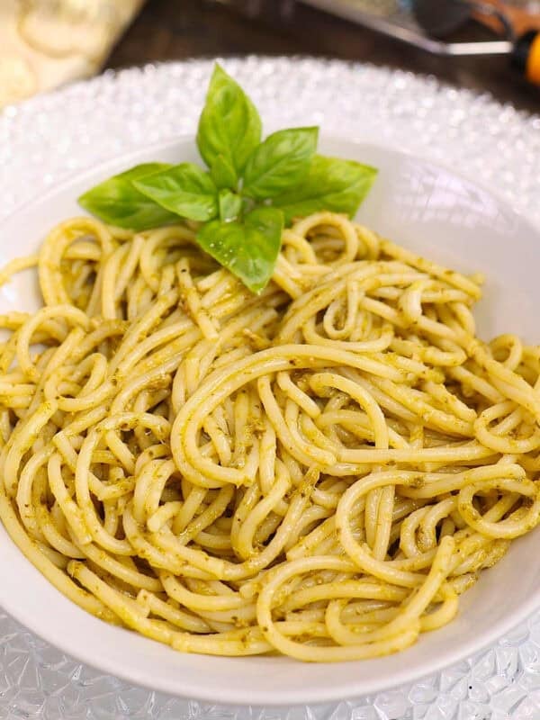 an overhead photo of a white bowl filled with pesto pasta on a silver tray.
