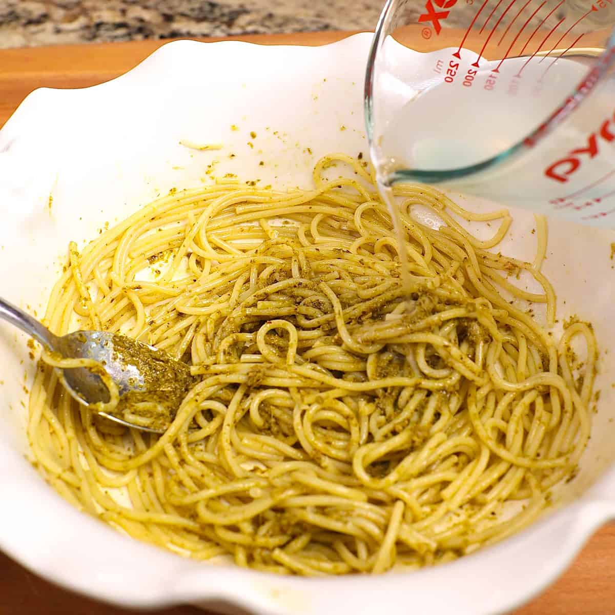 pasta water added to a bowl of pesto pasta.