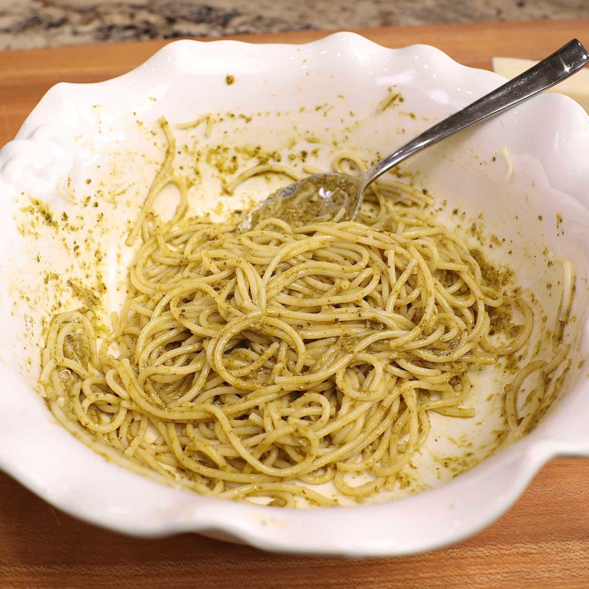 pesto pasta in a large white bowl with a spoon on the side.