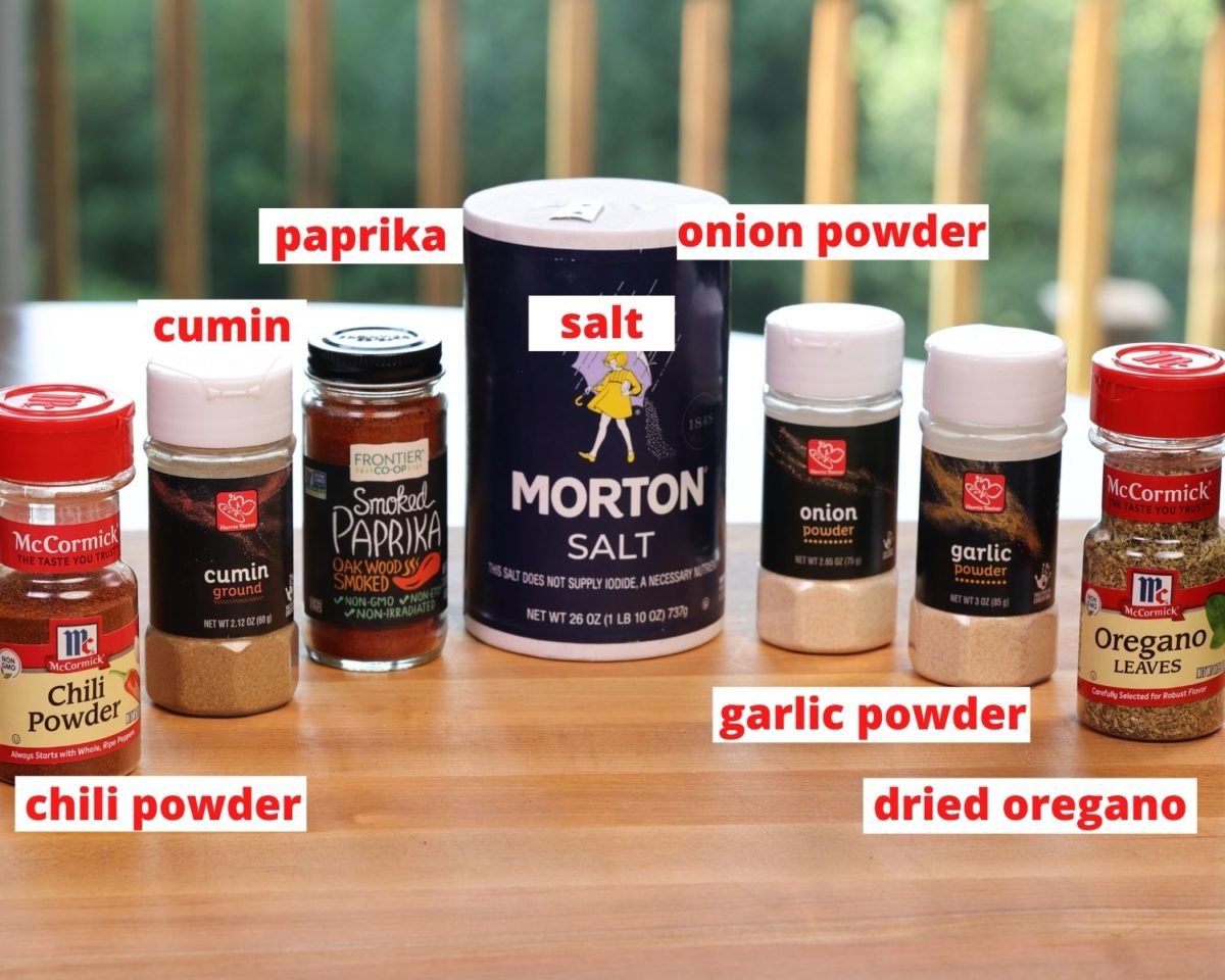 jars of garlic powder, onion powder, paprika, salt, cumin, and oregano on a brown table