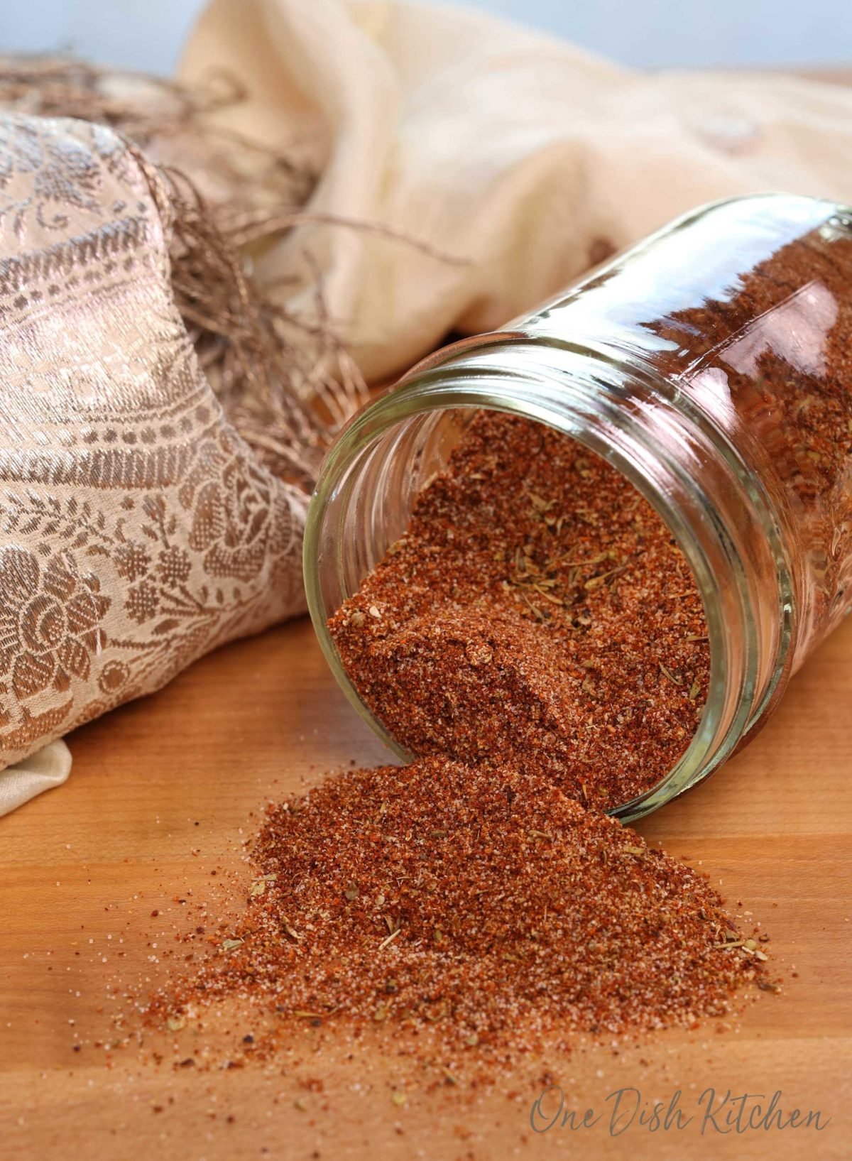 a mason jar filled with taco seasoning laying down on a brown cutting board with seasoning spilling out onto the board.