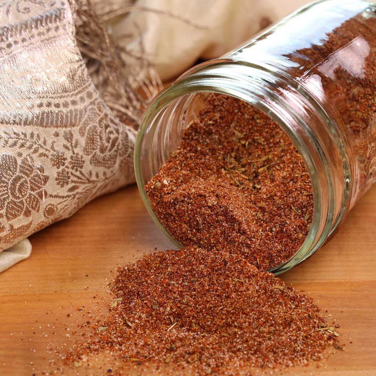 a mason jar filled with taco seasoning laying down on a brown cutting board with seasoning spilling out onto the board.