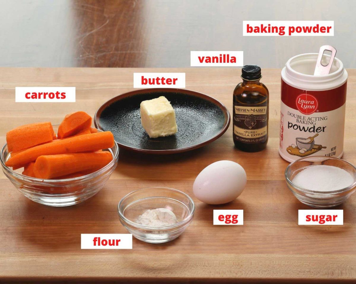 carrots, an egg, sugar, vanilla, baking powder, and other ingredients needed to make a mini carrot souffle on a wooden cutting board.