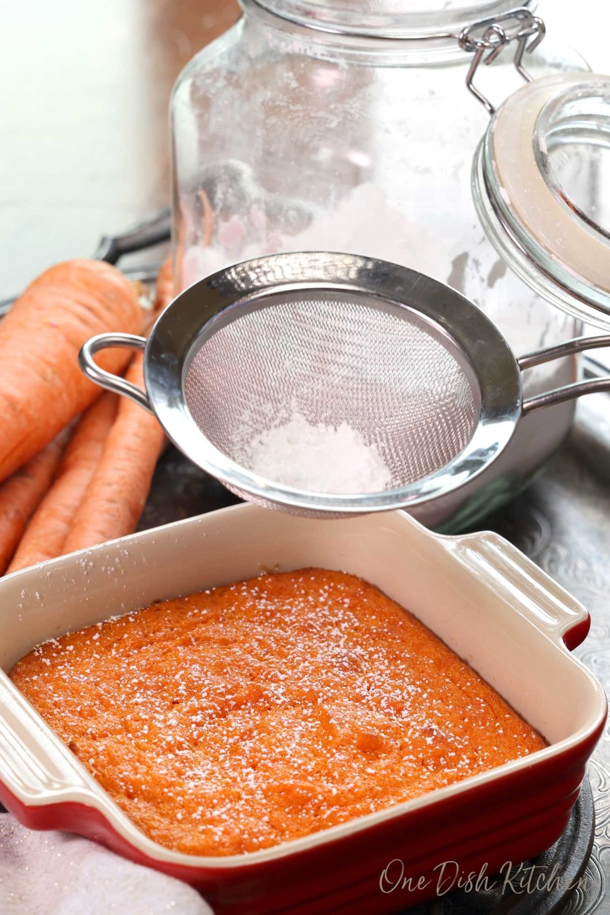 an individual carrot souffle on a silver tray next to a jar of powdered sugar.