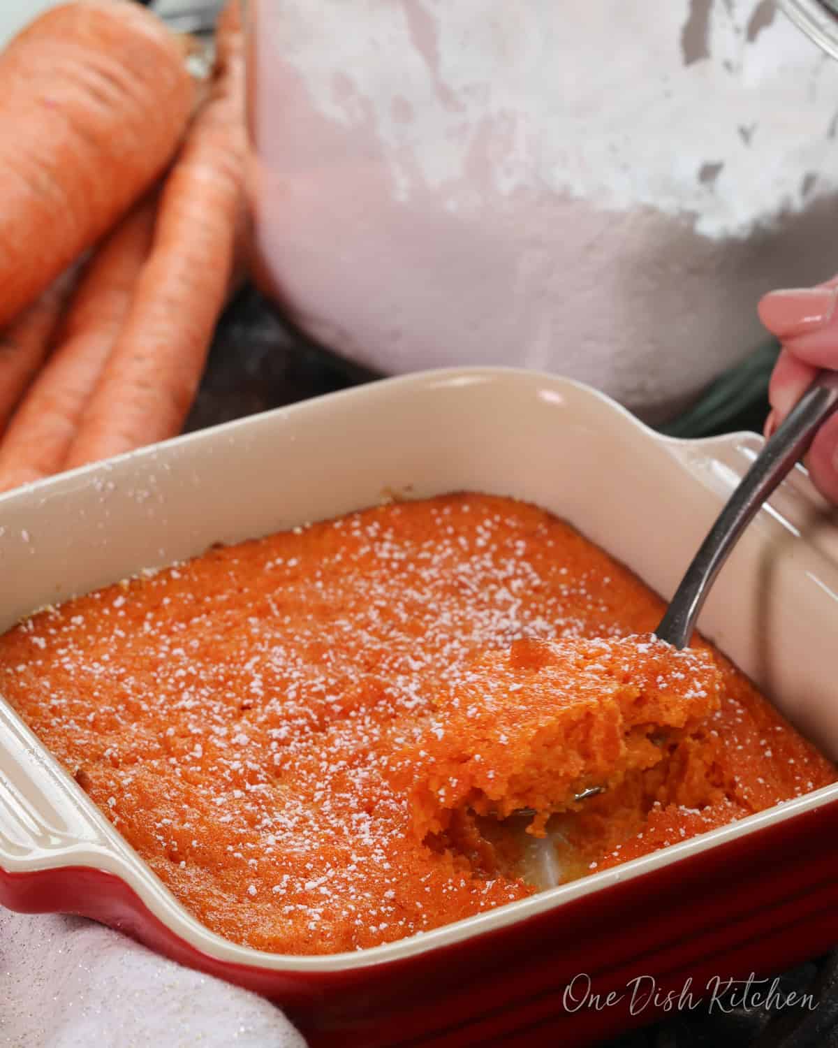 a mini carrot souffle in a small baking dish with a spoon on the side.