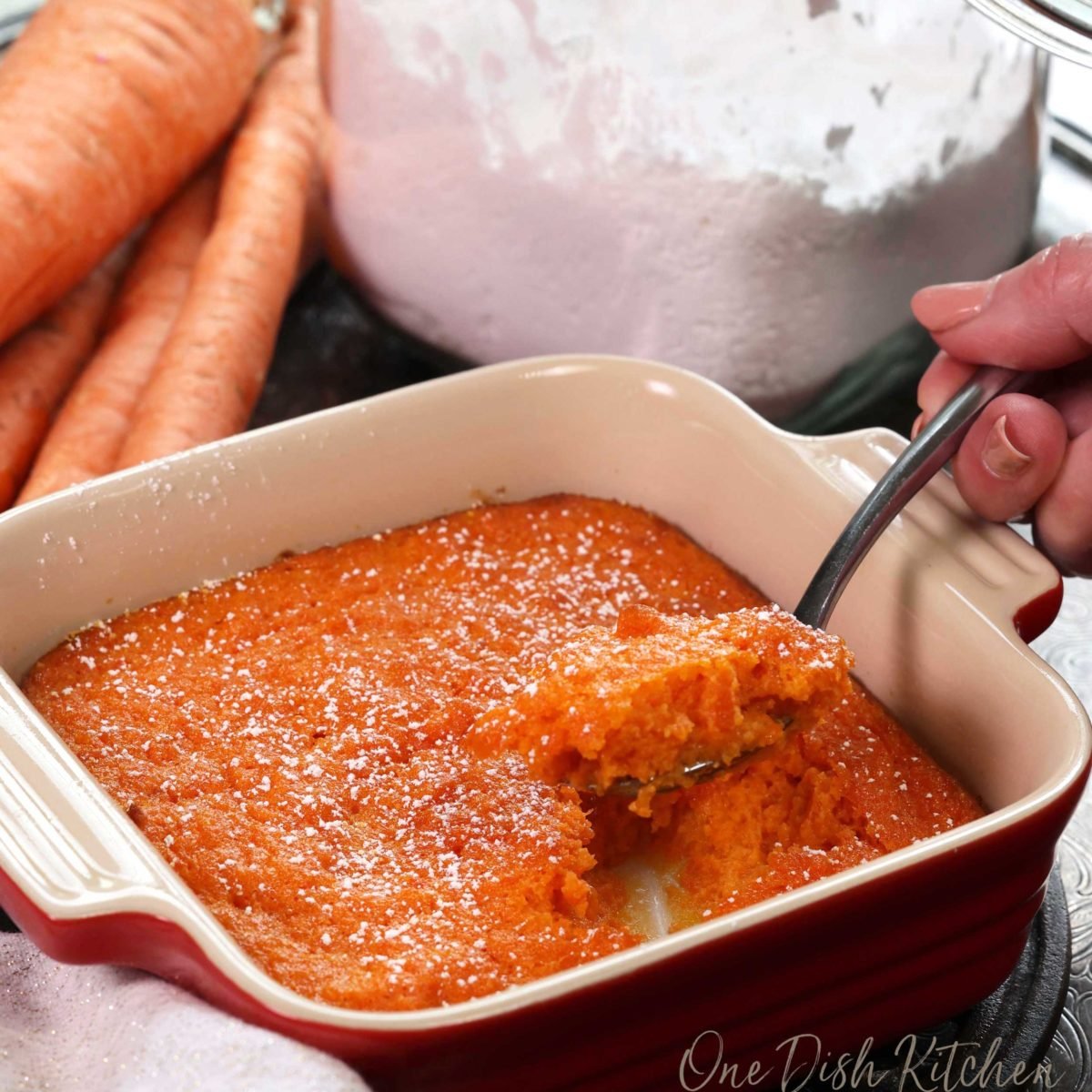 a spoonful of carrot souffle held above the baking dish containing the remainder.