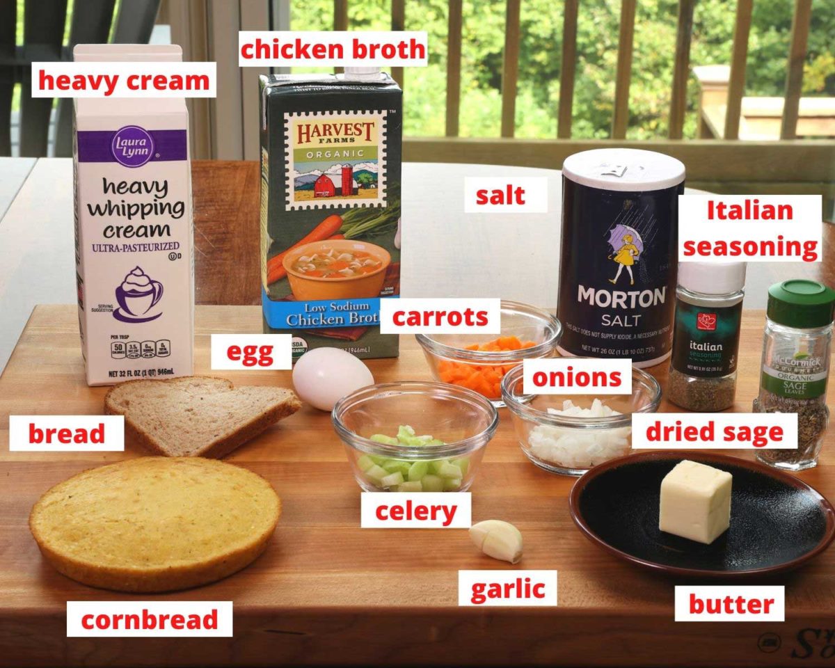 ingredients in cornbread dressing; cornbread, a slice of bread, cream, broth, and egg and seasonings on a wooden cutting board.