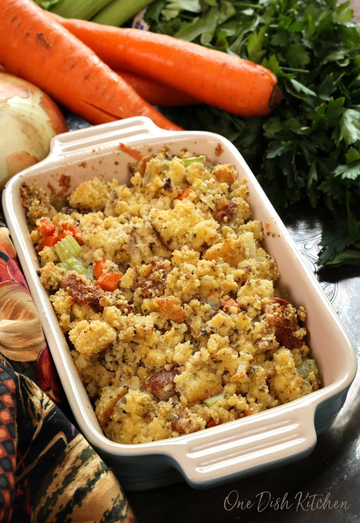 a baking dish filled with cornbread dressing on a silver tray next to carrots and onions.