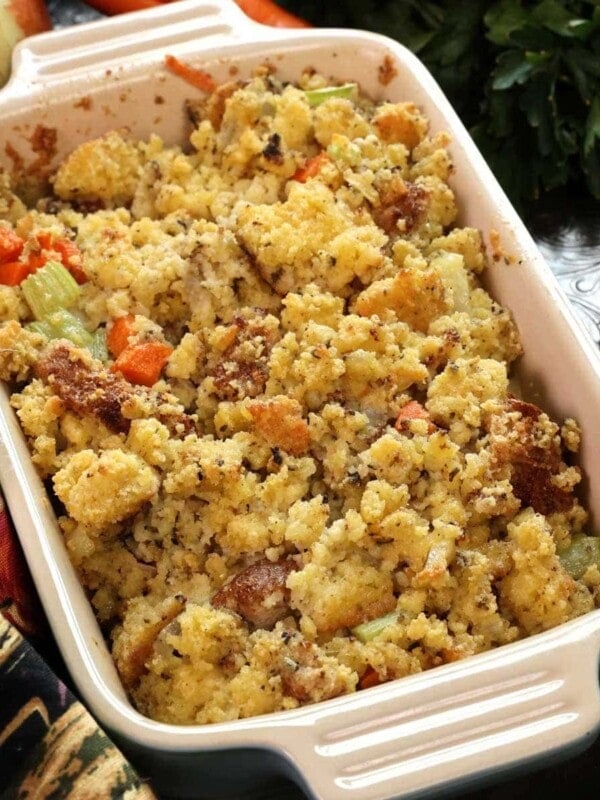 a baking dish filled with cornbread dressing on a silver tray next to carrots and onions