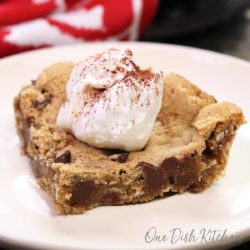 a slice of an oatmeal chocolate chip skillet cookie on a plate topped with whipped cream next to a red napkin