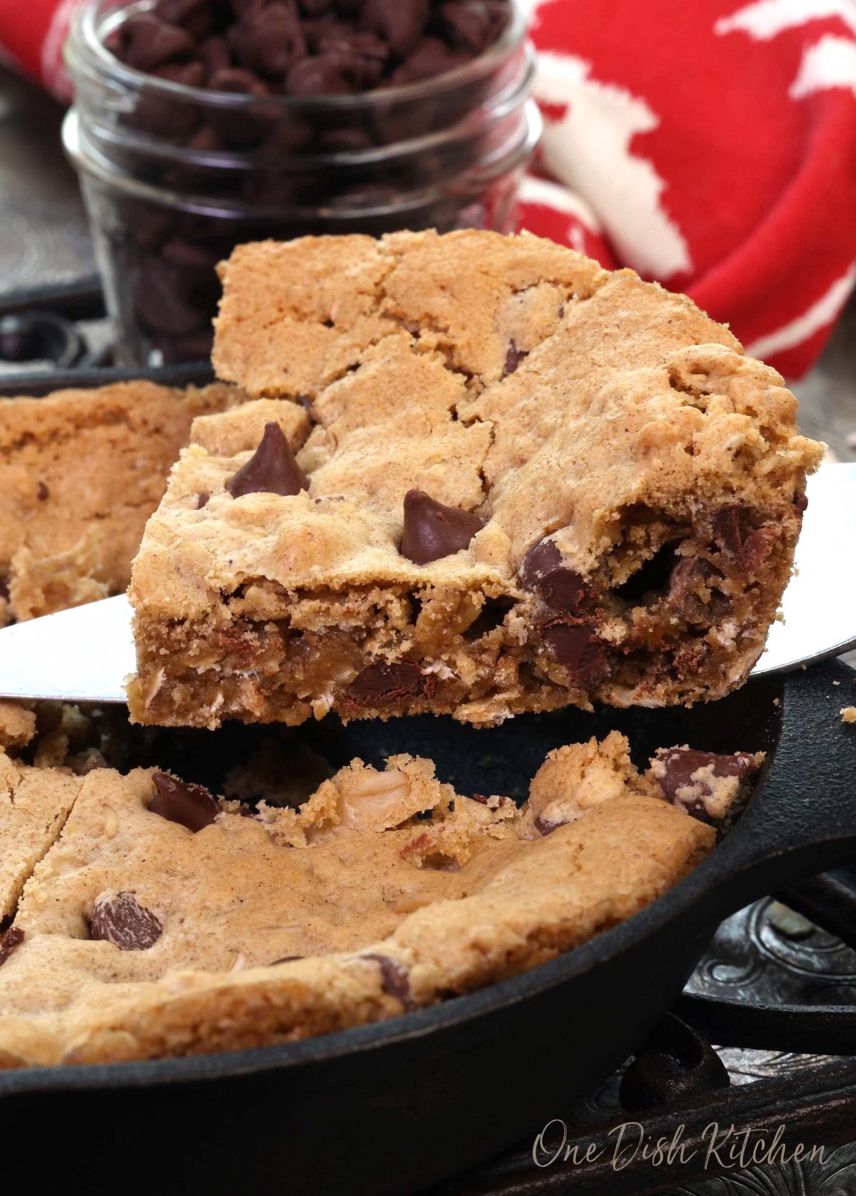 a slice of a chocolate chip oatmeal skillet cookie being transferred from the skillet to a plate.