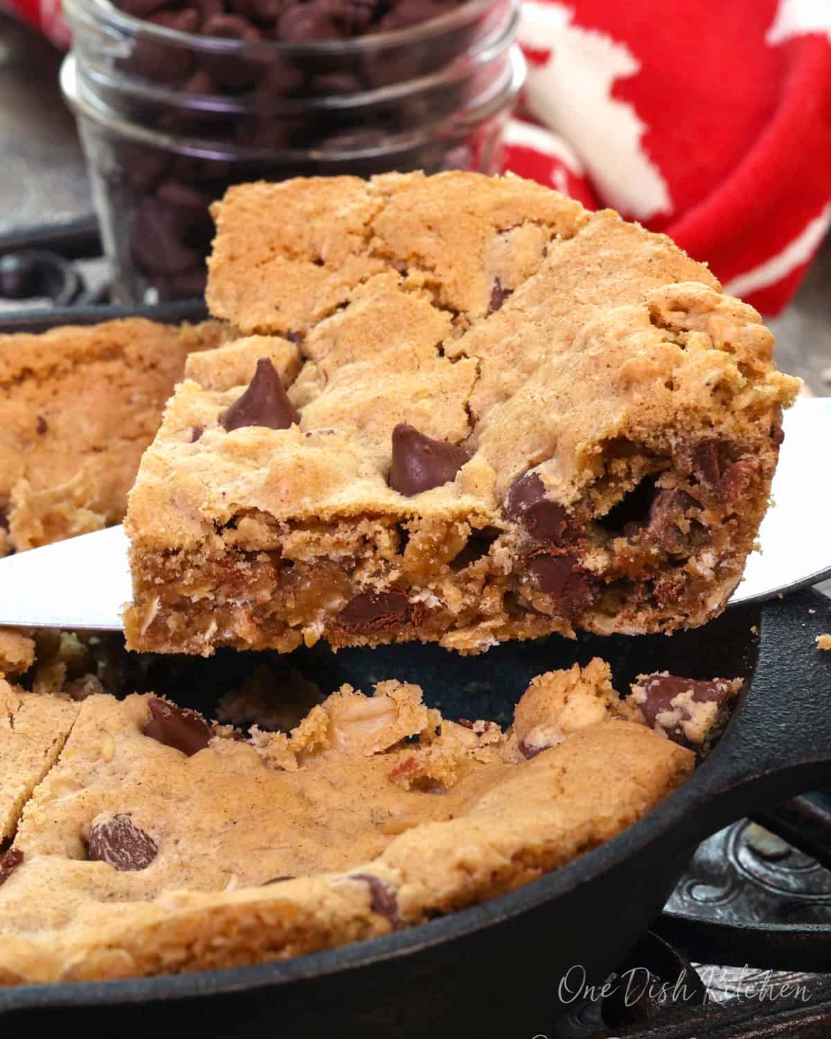 A wedge of a mini oatmeal chocolate chip skillet cookie being sliced and lifted from the skillet.