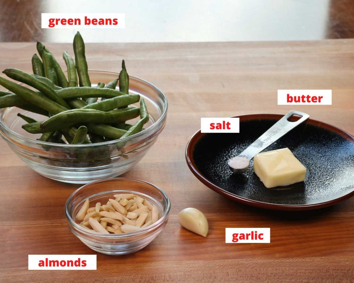 green beans, almonds, butter, garlic and salt on a wooden cutting board in a kitchen.