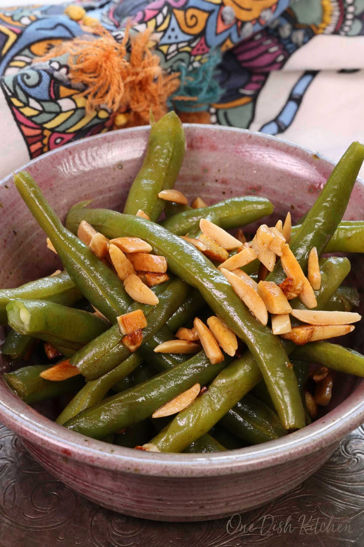 a pink bowl filled with cooked green beans topped with almonds.