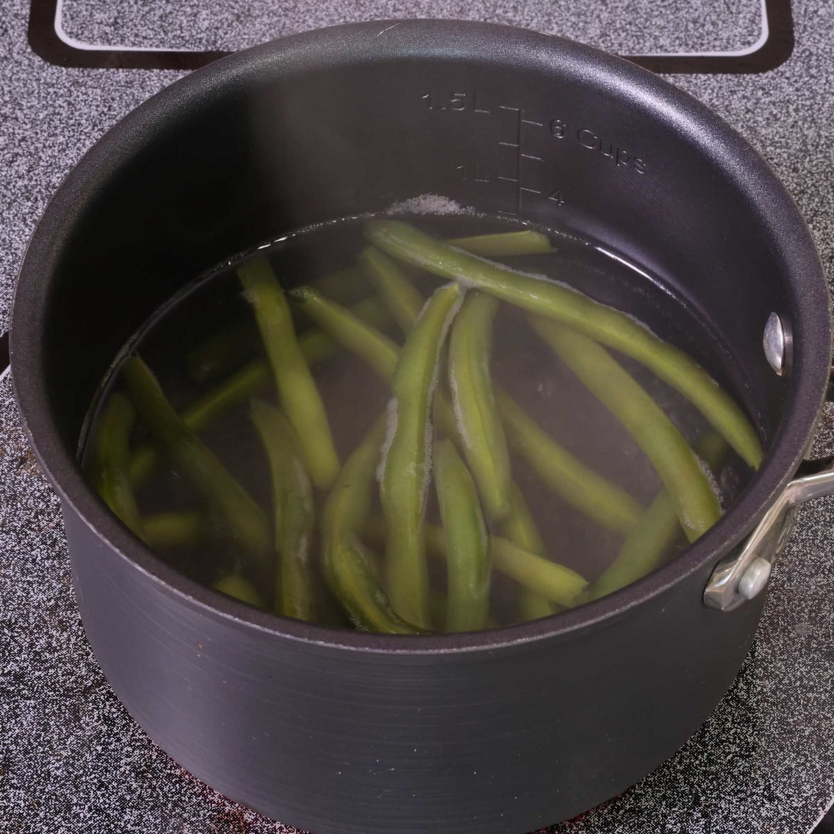a pot filled with green beans and water on a stove.