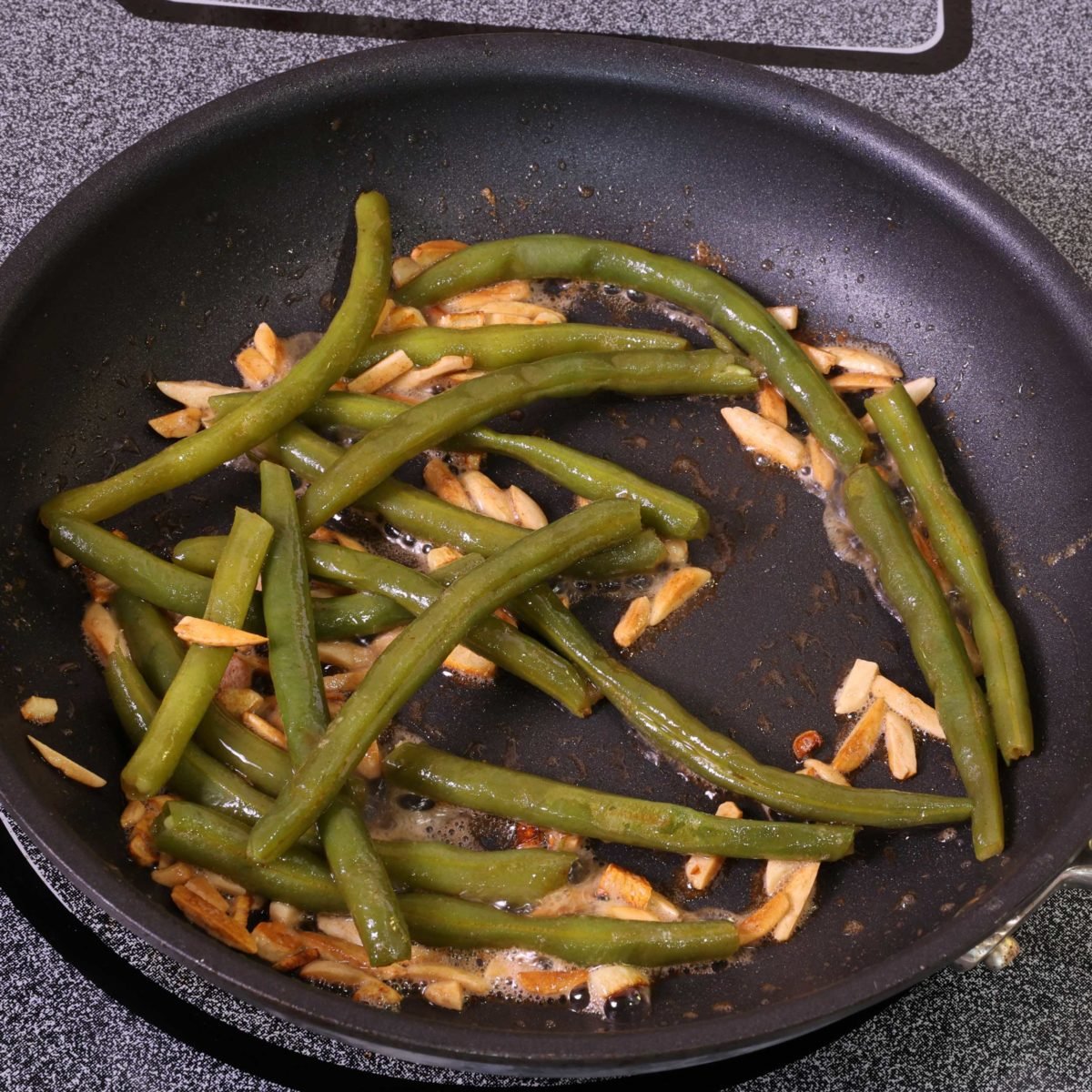 fresh green beans cooking in a skillet with garlic and almonds.