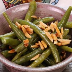 a pink bowl filled with cooked green beans topped with almonds