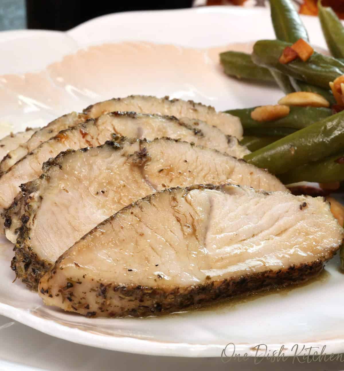 sliced oven roasted turkey tenderloin on a white plate next to green beans.
