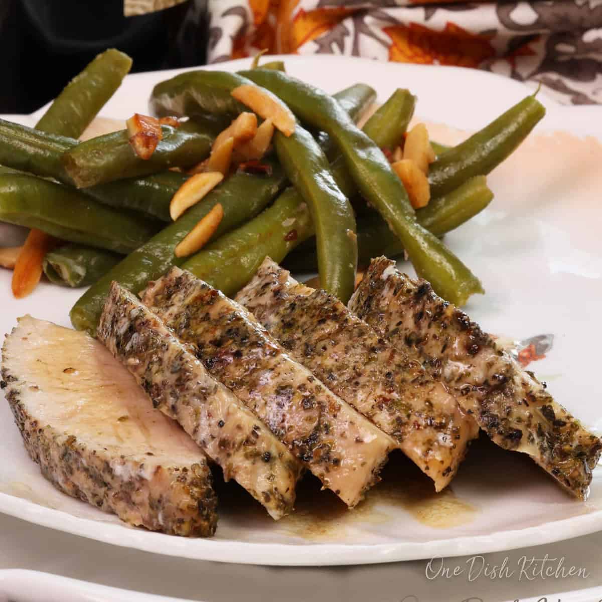 sliced turkey tenderloin on a plate next to green beans.