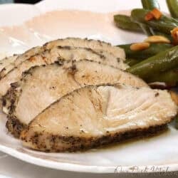 sliced oven roasted turkey tenderloin on a white plate next to green beans.