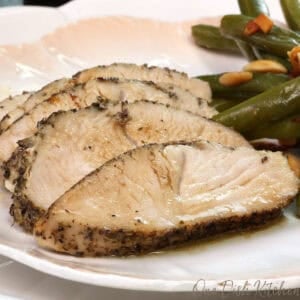 sliced oven roasted turkey tenderloin on a white plate next to green beans.