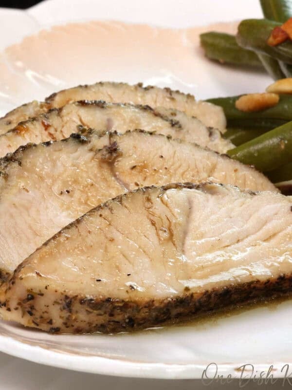 sliced oven roasted turkey tenderloin on a white plate next to green beans.