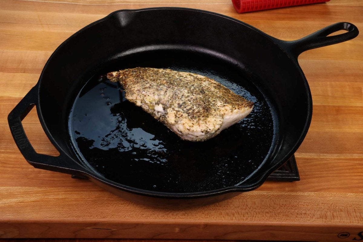 a partially cooked turkey tenderloin in a cast iron skillet next to tongs.