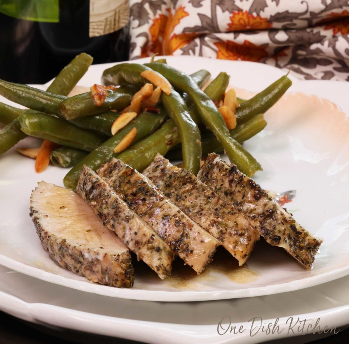 slices of turkey tenderloin on a white plate next to green beans and a bottle of wine.