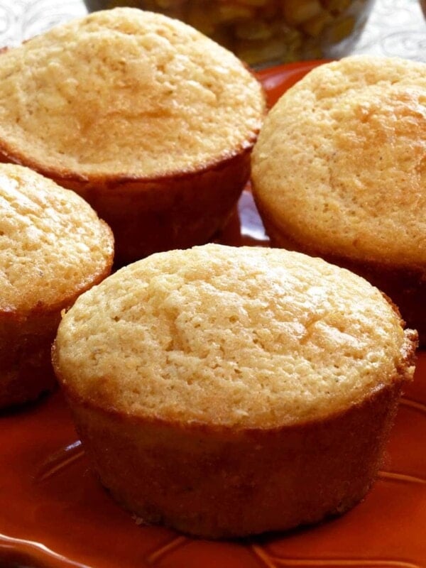 four corn muffins on a plate next to a bowl of corn