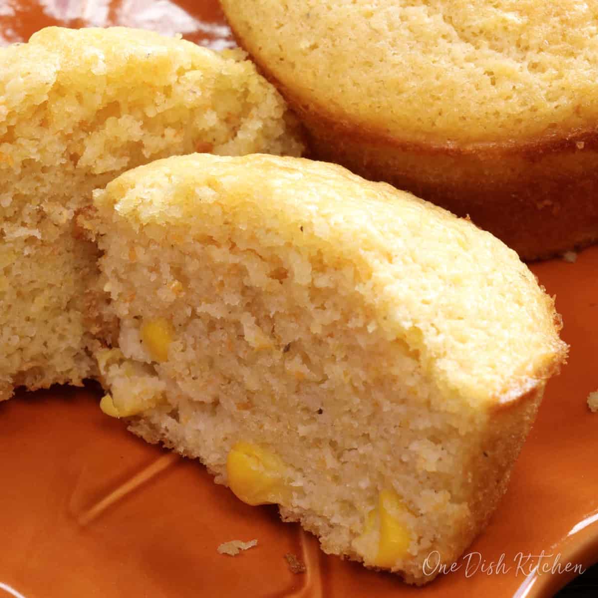 a corn muffin on an orange plate cut in half.