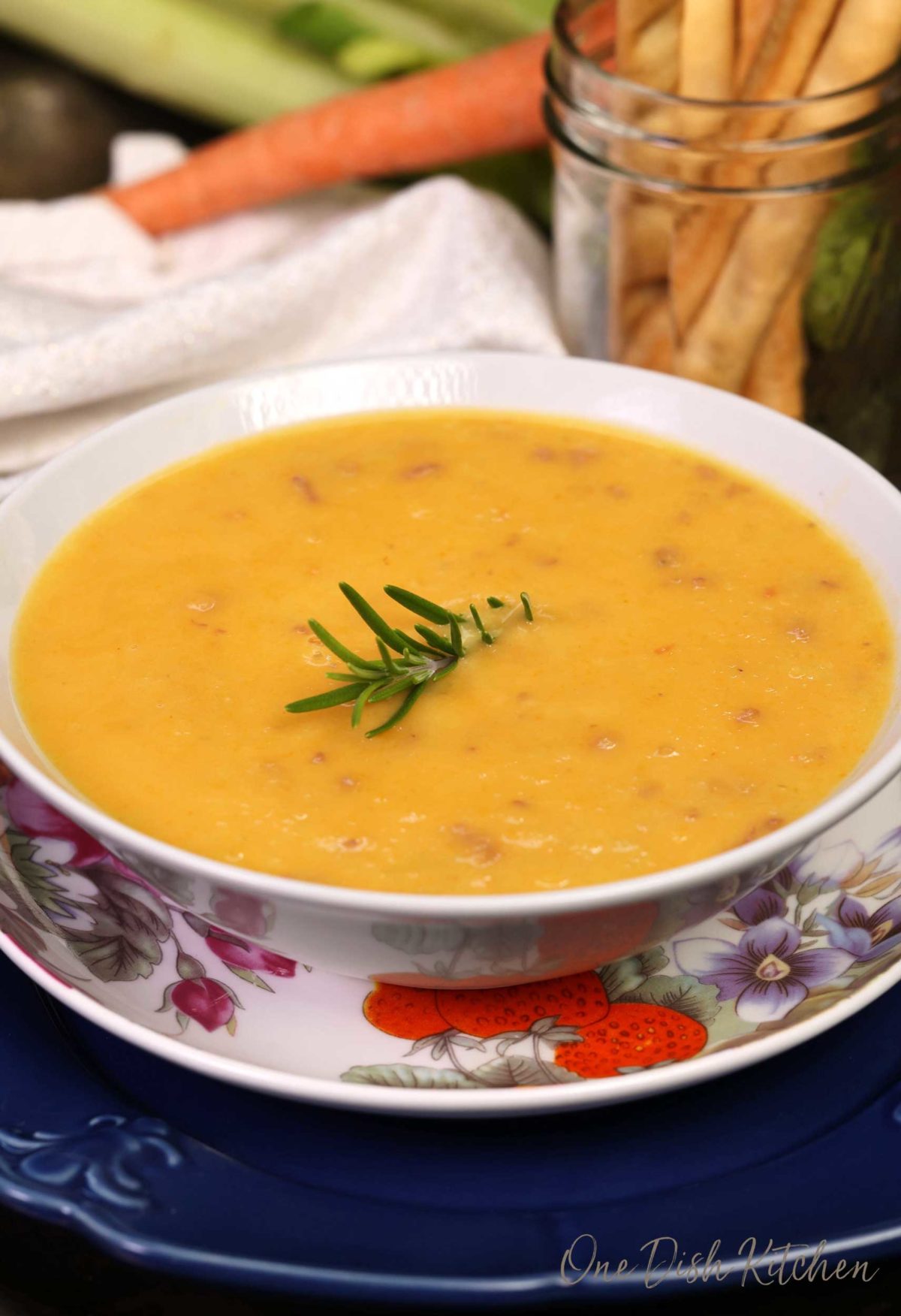 a white bowl filled with creamy vegetable soup with fresh rosemary on top.