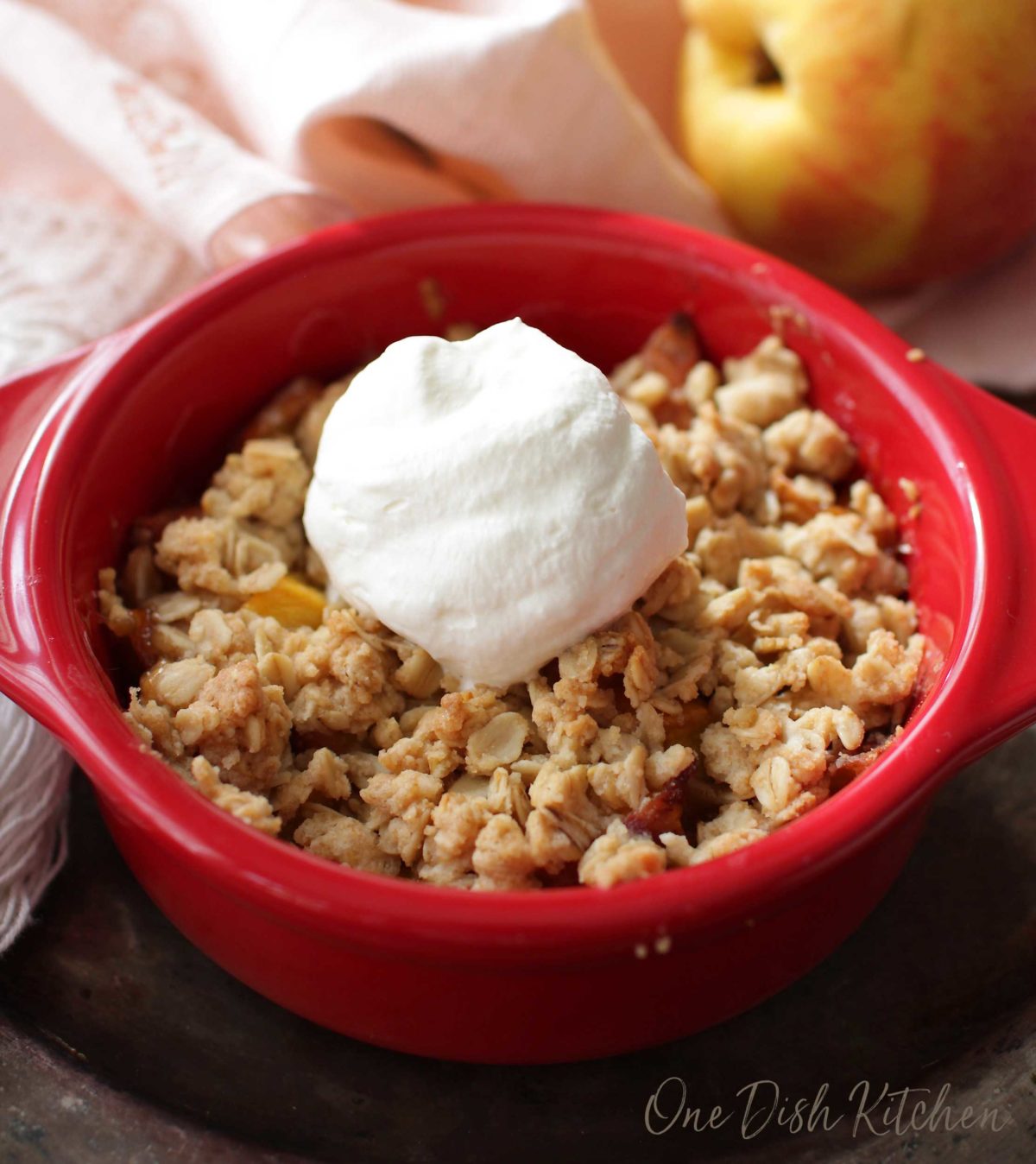 a peach crisp topped with whipped cream in a red bowl.