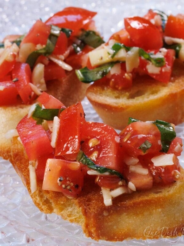 a piece of tomato and basil bruschetta on a white plate next to a bowl of chopped tomatoes