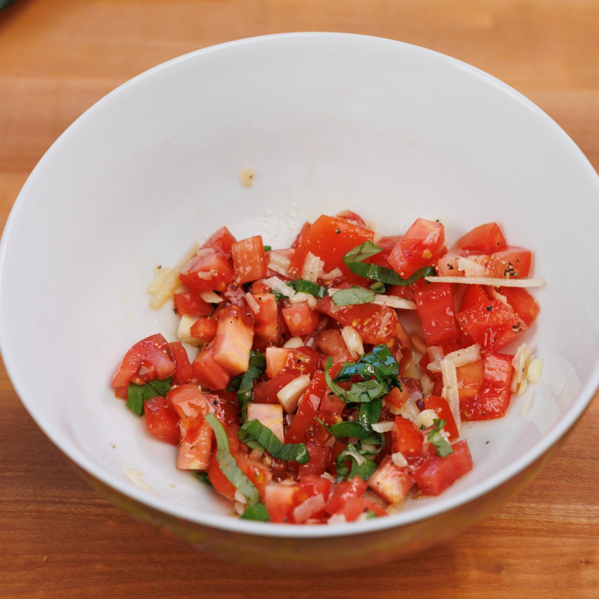 fresh basil, chopped tomatoes and garlic in a small white bowl.