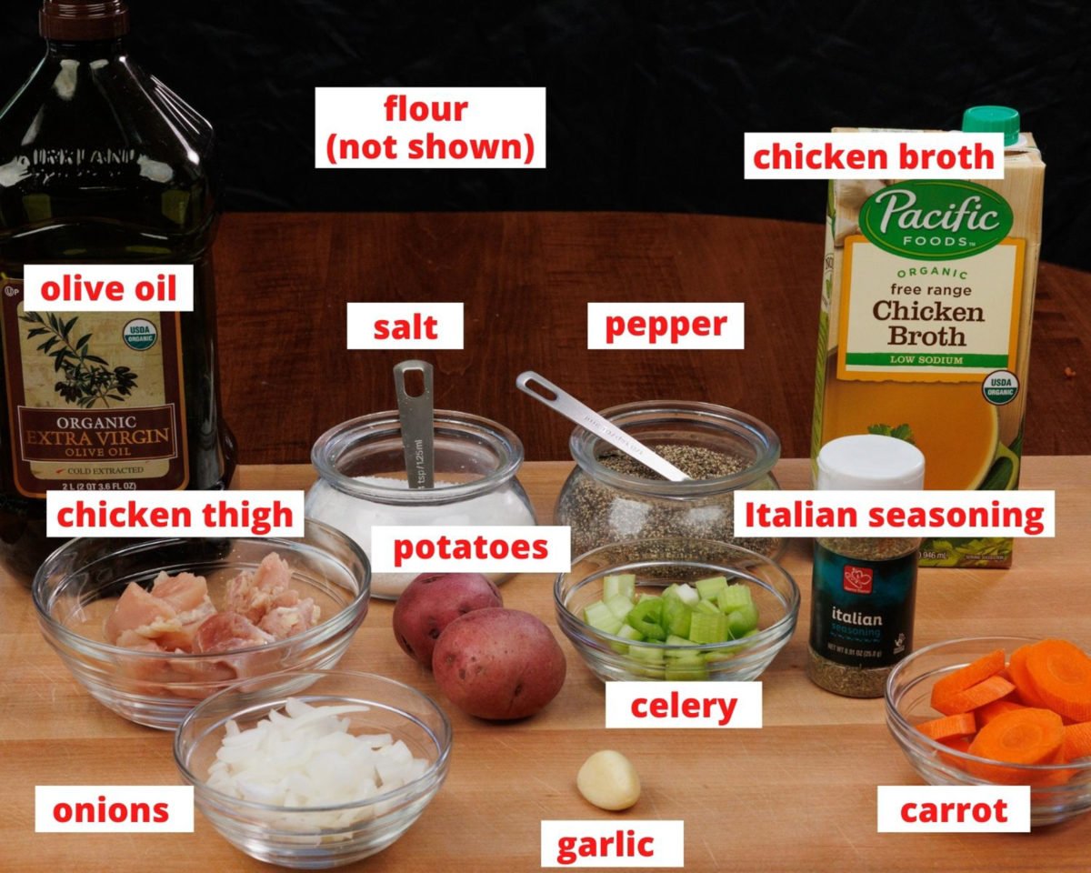 the ingredients in chicken stew on a wooden cutting board: chicken, broth, vegetables, olive oil, and seasonings.