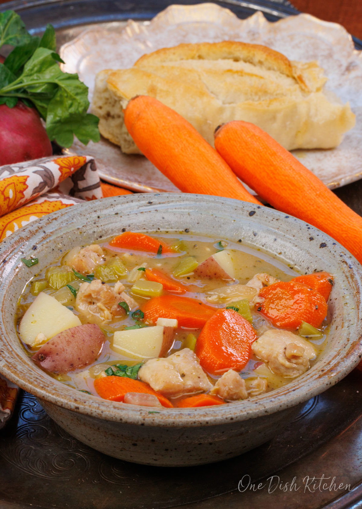 a blue bowl filled with chicken stew next to a plate with a loaf of french bread.