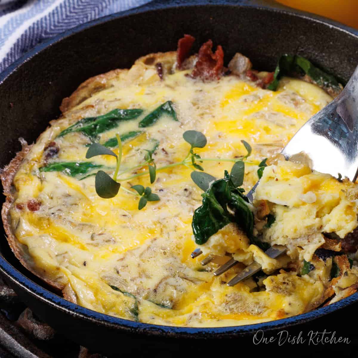 a mini frittata with a forkful of spinach and egg on the side of the skillet.