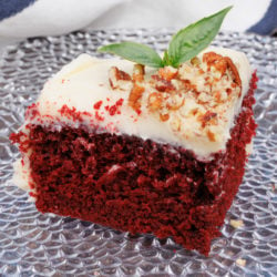 a slice of red velvet cake with cream cheese frosting and a sprig of fresh mint on a clear plate