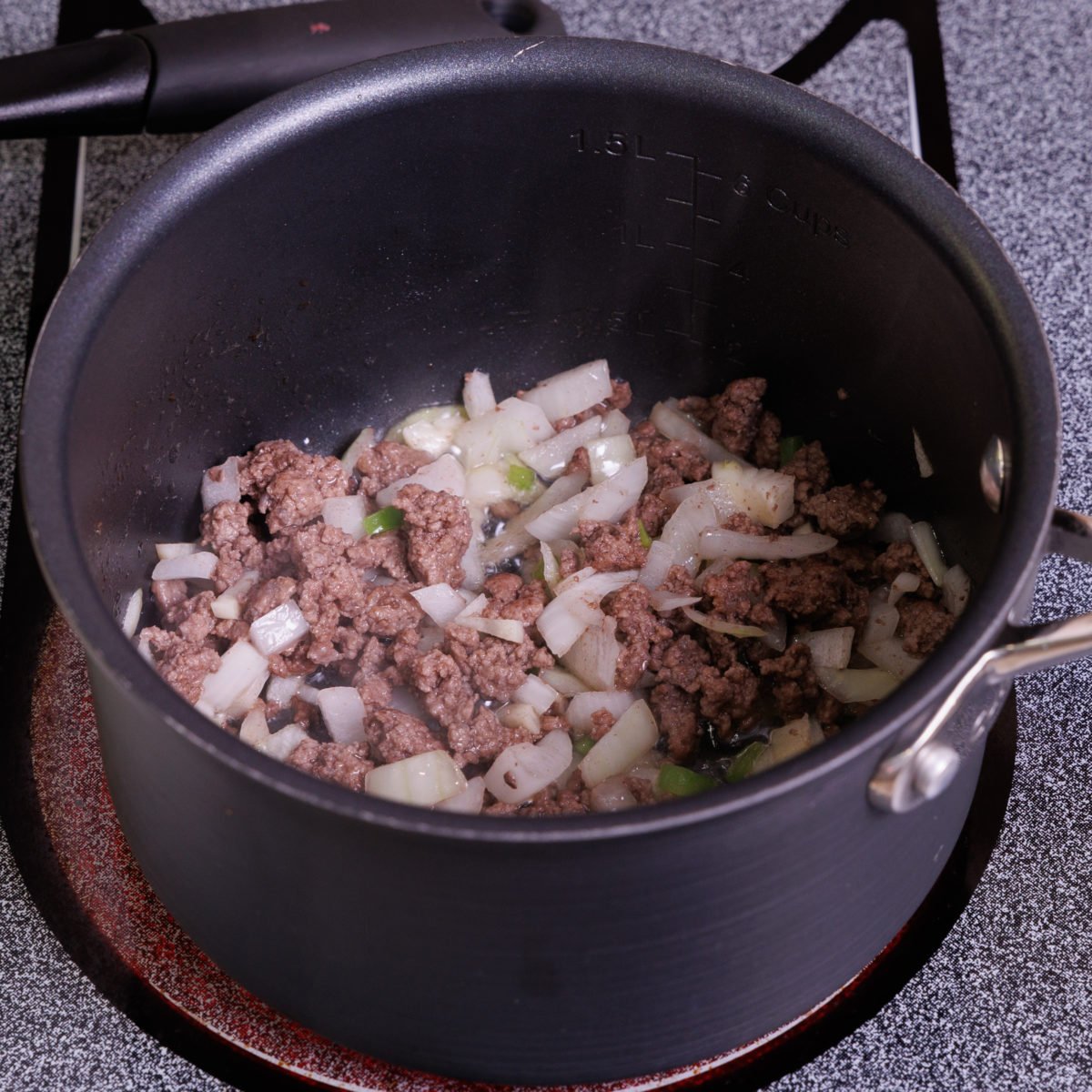 ground beef, onions, and garlic in a small black pot.