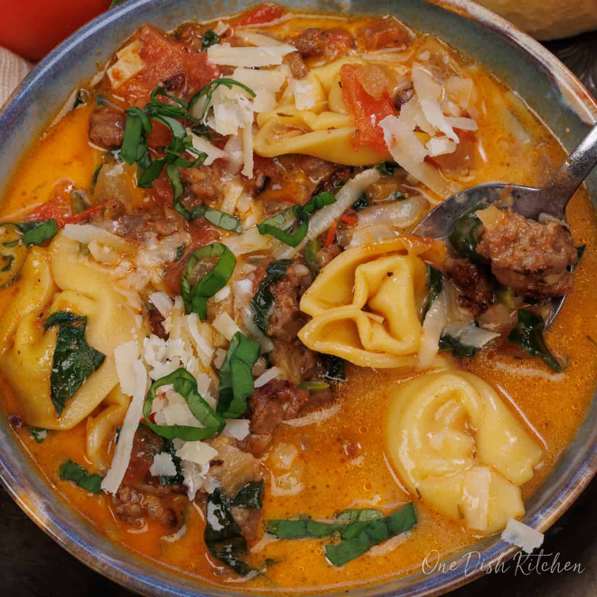 a spoonful of tortellini and sausage over a bowl of tortellini soup.