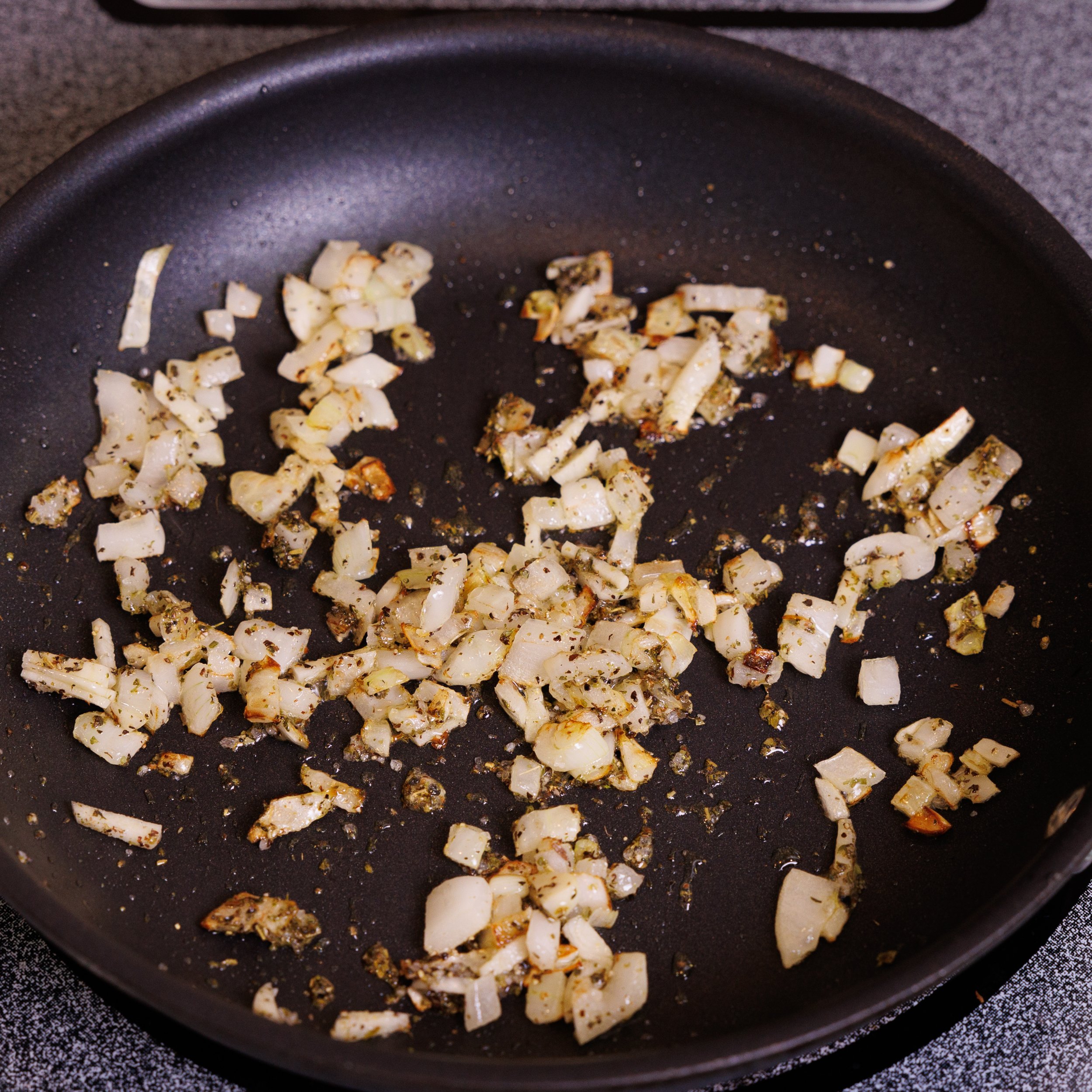 onions, garlic, and seasonings in a small frying pan on a stove.