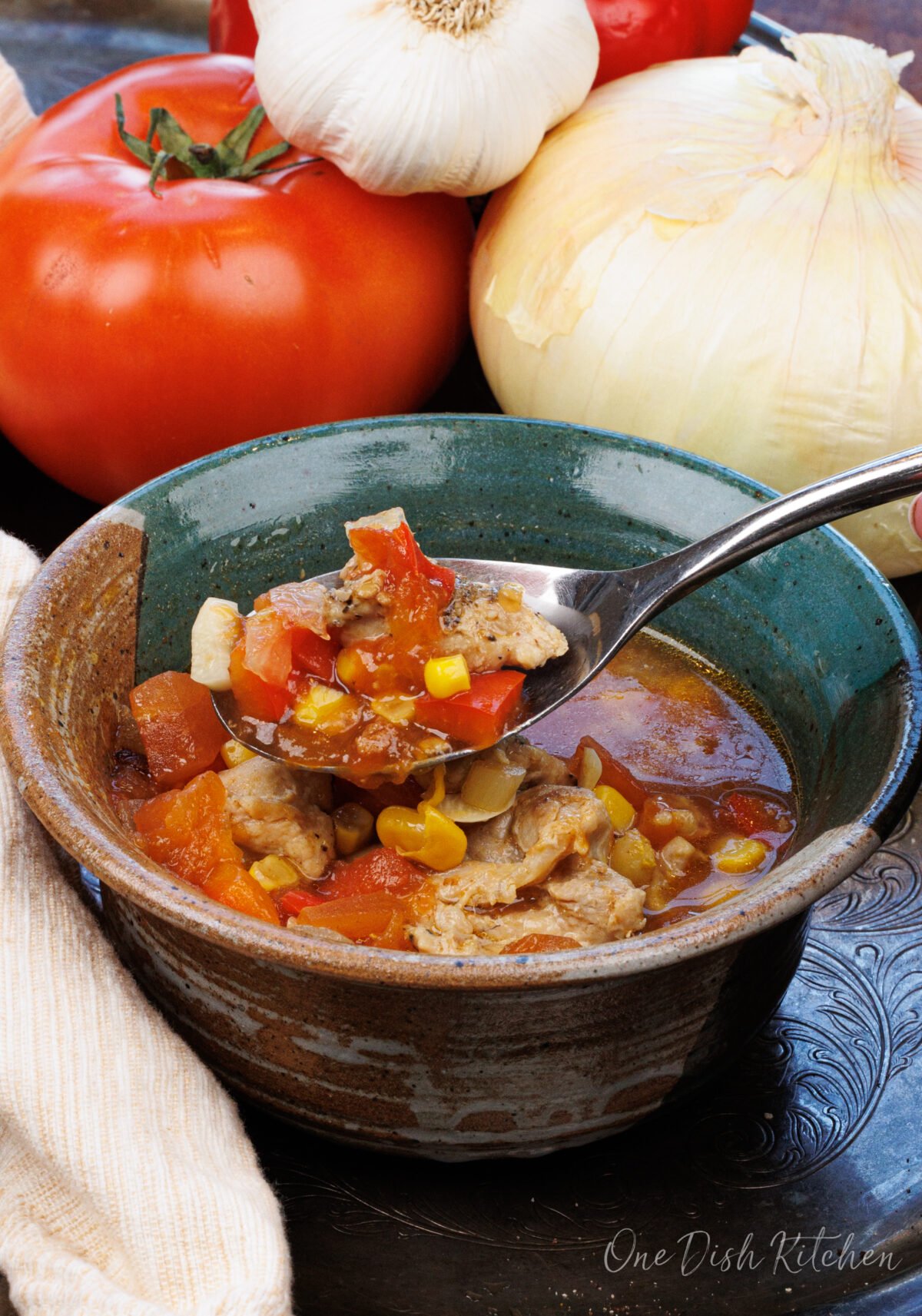 a bowl of chicken tortilla soup with a spoon on the side next to tomatoes and onions.