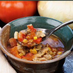 a bowl of chicken tortilla soup with a spoon on the side next to tomatoes and onions