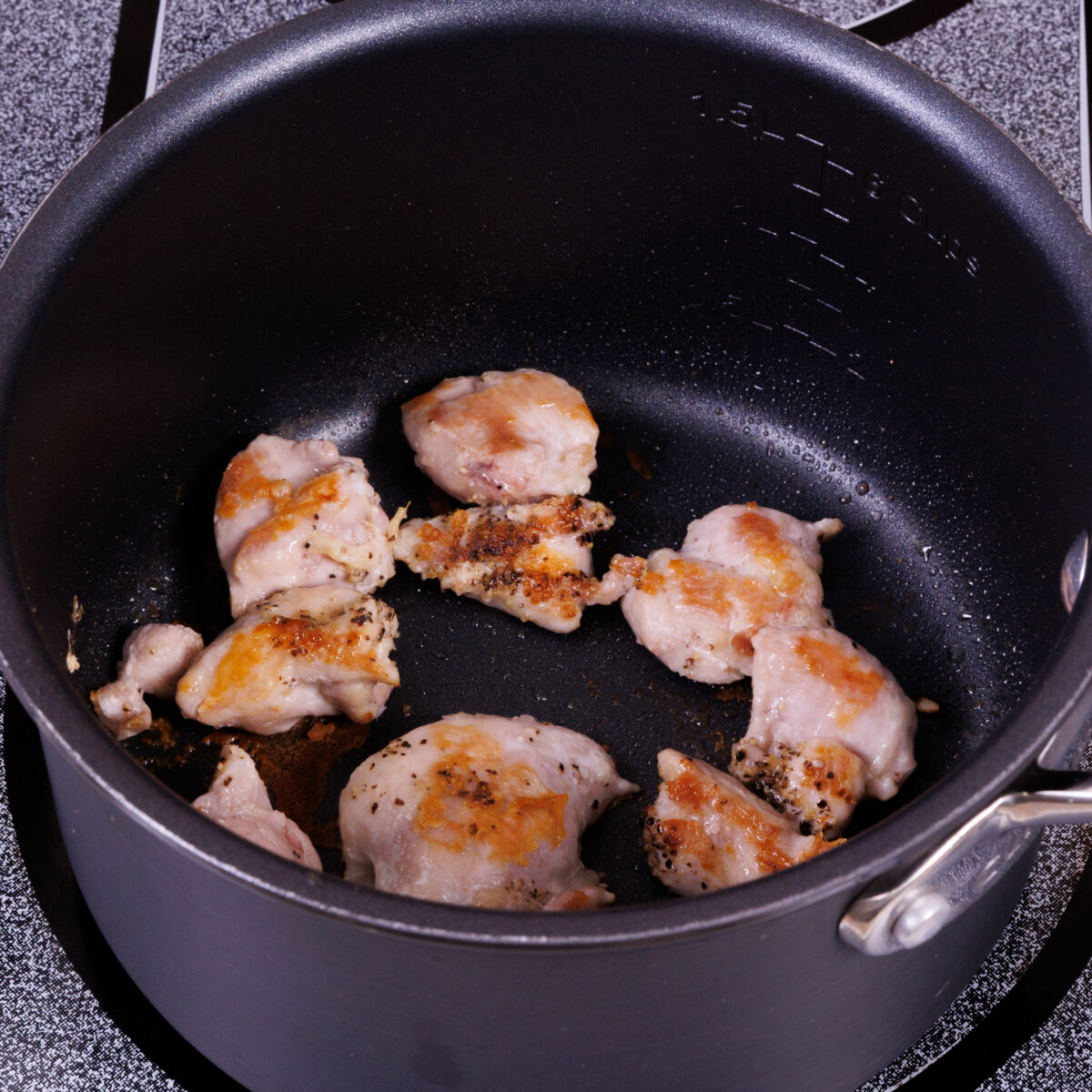 chicken pieces cooking in a small pot.