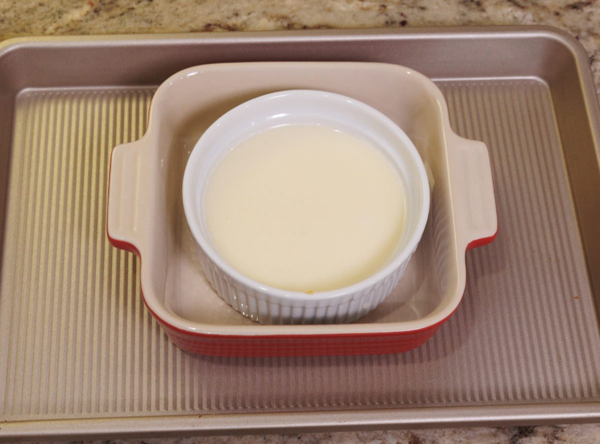 a unbaked custard in a small ramekin inside a larger baking dish.