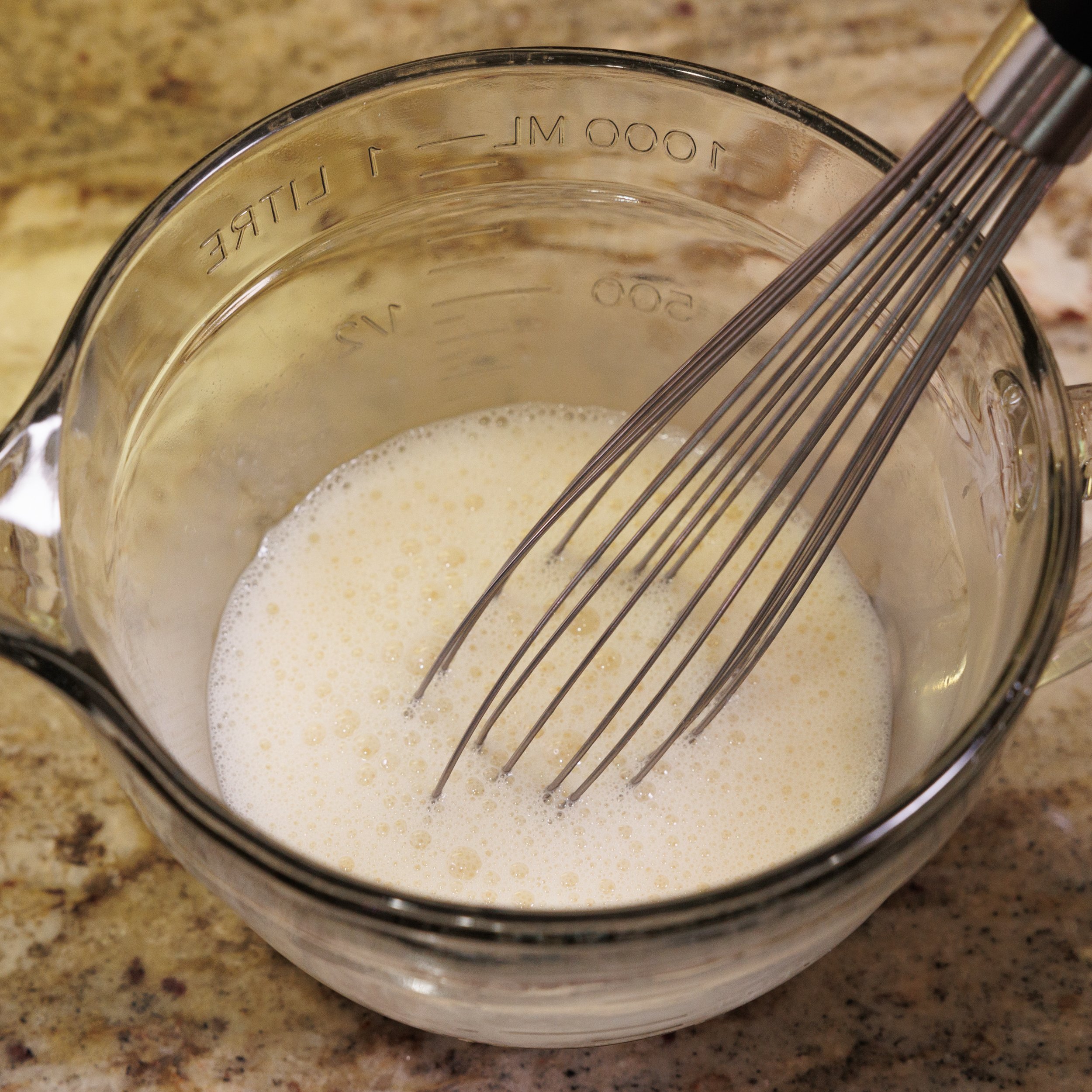 egg and milk in a mixing bowl next to a wire whisk.