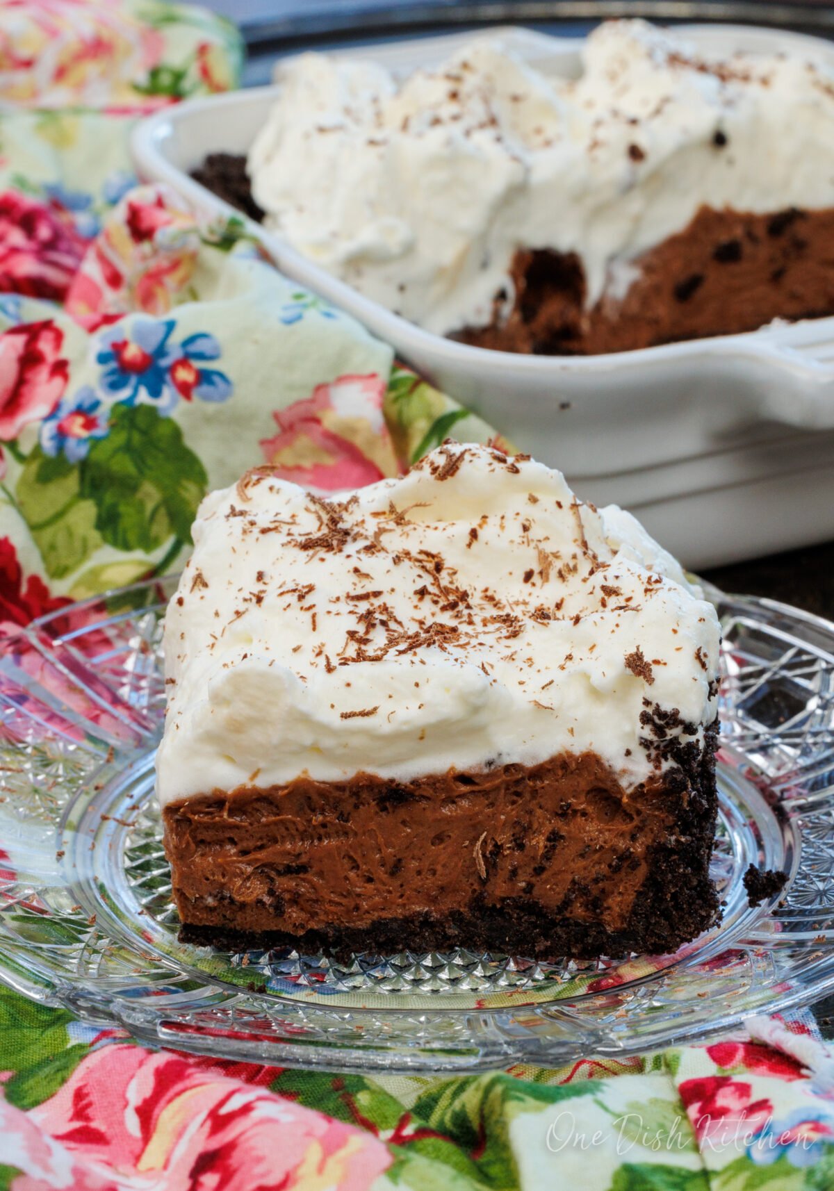 a slice of french silk pie on a clear plate next to the full pie in the background.