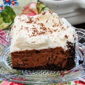 a slice of french silk pie on a clear plate next to the full pie in the background.