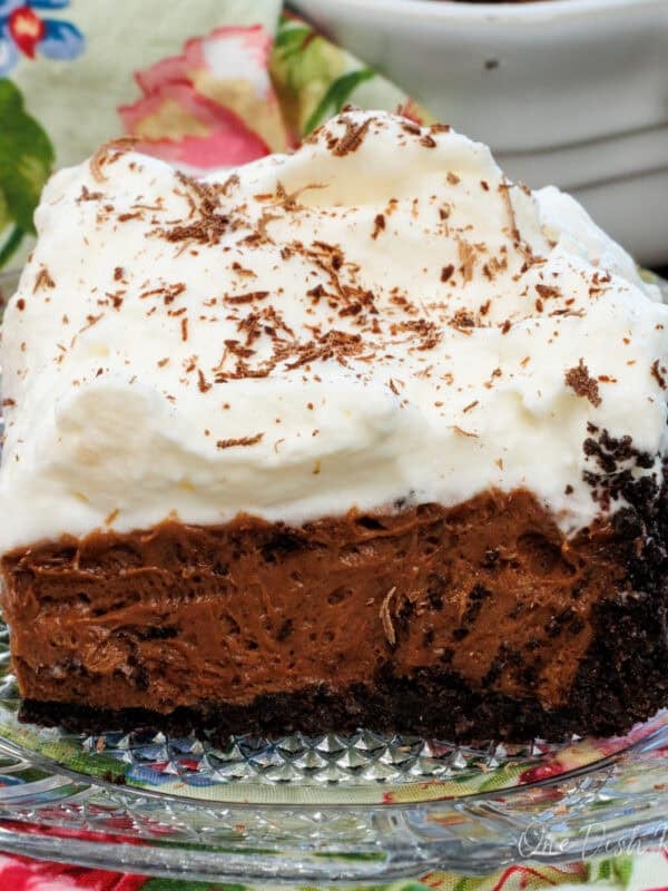 a slice of french silk pie on a clear plate next to the full pie in the background.
