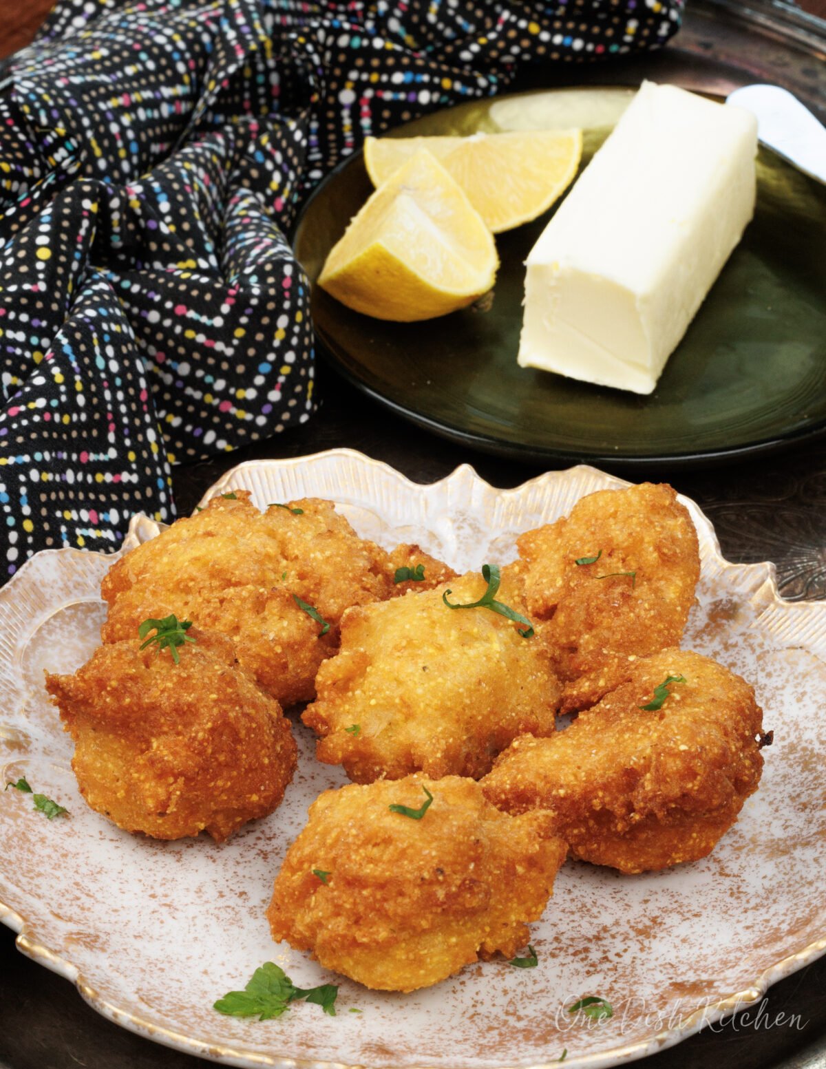 a plate of hush puppies next to a plate with butter on a silver tray.